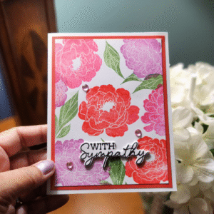 offer a message of comfort and support with this beautiful handmade "with sympathy" card. the design features a stunning pattern of hand stamped or painted flowers in gentle shades of pink, red, and purple, complemented by soft green leaves. the vibrant yet respectful color palette is a beautiful and thoughtful way to honor a loved one and let someone know you are thinking of them during a difficult time. the simple, elegant layout and the clear, heartfelt sentiment make this card a perfect expression of care and condolences.